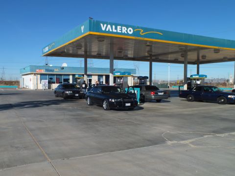 2003 Ford Crown Victoria - Black sedan with front plate parked at a Valero station as a group gathers near the fuel pumps