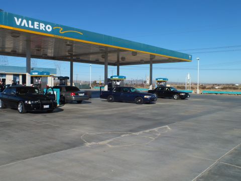 2003 Ford Crown Victoria - Multiple dark sedans lined up at a Valero station, transmission towers and open desert in the background