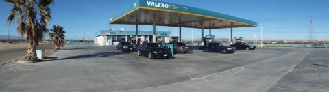 2003 Ford Crown Victoria - Wide panorama of a Valero station canopy with several dark sedans, palms and open desert all around