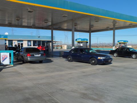 2003 Ford Crown Victoria - Gray sedan and dark blue sedan parked under a fuel canopy beside a CFN card-lock sign, towers beyond