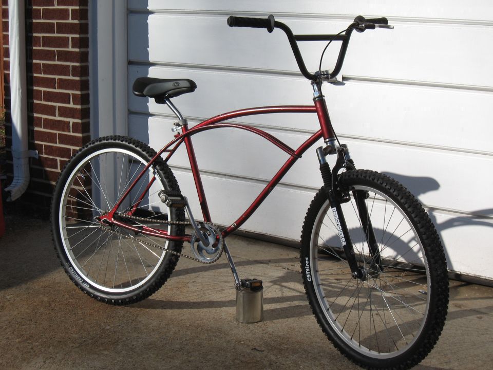 red cruiser bike with black handlebars and tires, parked in front of a garage door