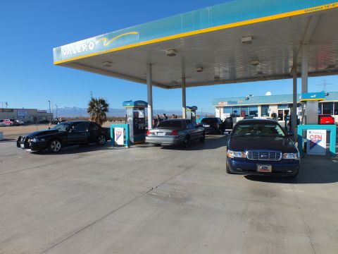 2003 Ford Crown Victoria - Row of black and dark blue sedans under a Valero canopy, palm tree and pale mountains in the background