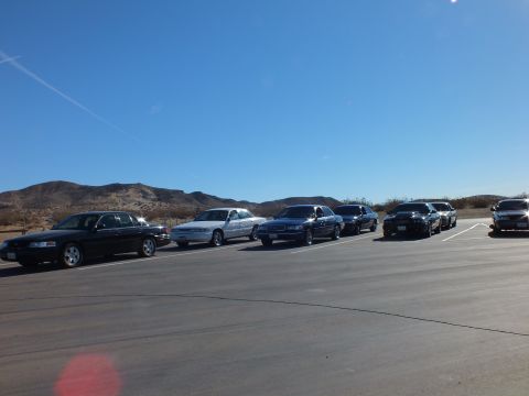 2003 Ford Crown Victoria - Several sedans angled in a paved lot under deep blue sky with low desert hills along the horizon