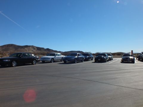 2003 Ford Crown Victoria - Row of sedans facing the camera in a wide paved desert lot with low brown hills beyond