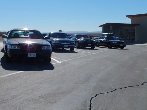 2003 Ford Crown Victoria - Black four-door sedan parked at an angle ahead of several other dark cars next to a concrete building