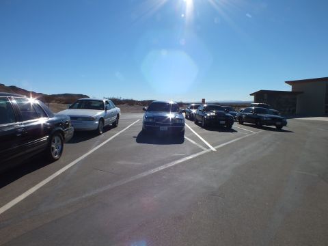 2003 Ford Crown Victoria - Mixed lineup of dark and white sedans parked on pavement near desert hills