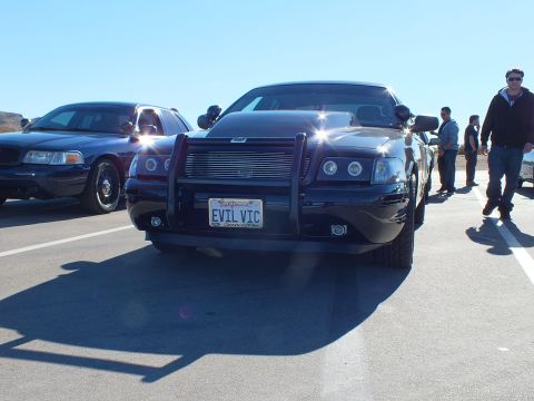 2003 Ford Crown Victoria - Black Charger with chrome grille and EVIL VIC plate as a man passes on the lot