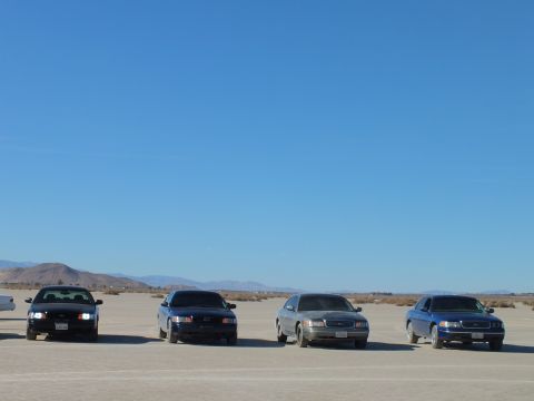 2003 Ford Crown Victoria - Four dark and silver sedans spaced across a flat desert dry lake bed