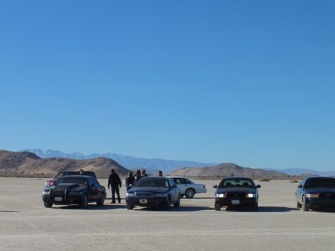 2003 Ford Crown Victoria - Row of sedans on a desert flat with bystanders and distant snowy mountains