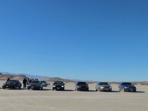 2003 Ford Crown Victoria - Lineup of six sedans across a desert dry lake with people at the left end