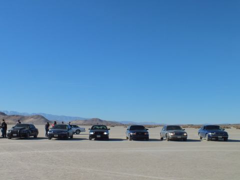 2003 Ford Crown Victoria - Lineup of sedans on a desert flat, people and a silver car in the background