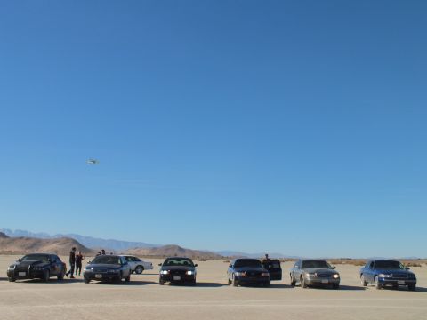 2003 Ford Crown Victoria - Lineup of sedans on a desert flat with a distant paraglider overhead