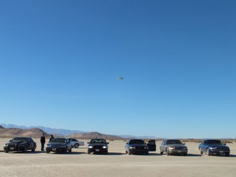 2003 Ford Crown Victoria - Row of sedans on a desert flat, bystanders and a small paraglider above