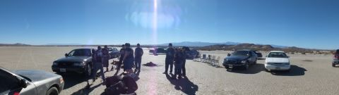 2003 Ford Crown Victoria - Panoramic desert flat with several sedans and a crowd of people; distant mountains line the horizon under sun glare.