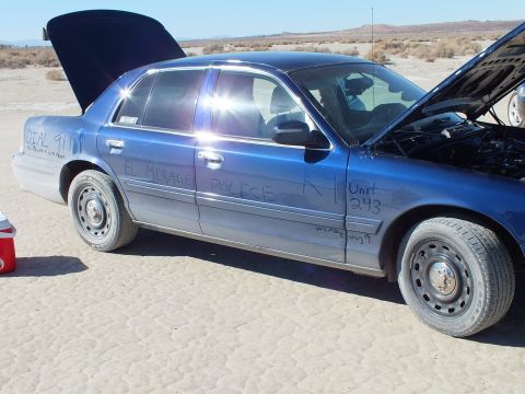2003 Ford Crown Victoria - Side of a blue Crown Victoria hand-marked EL MIRAGE POLICE, K9 Unit 243; hood open on the desert flat.