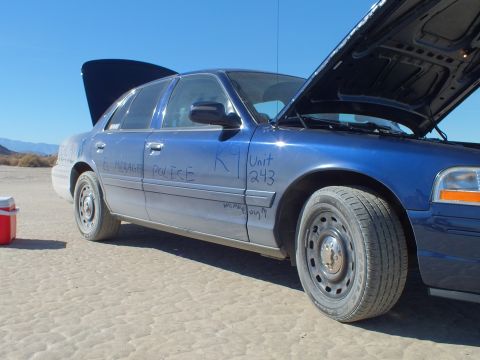 2003 Ford Crown Victoria - Close side view of a blue Crown Victoria scrawled EL MIRAGE POLICE, K9 Unit 243, hood raised on the lakebed.