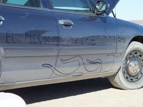 2003 Ford Crown Victoria - Side panel of a dusty blue sedan tagged in dust with EL MIRAGE POLICE K9 Unit 243 above a steel wheel.