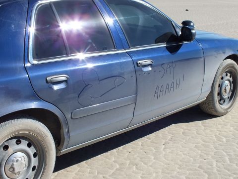 2003 Ford Crown Victoria - Side of a blue sedan with dust-drawn graphic and SAY AAAAH written in the grime above a steel wheel.