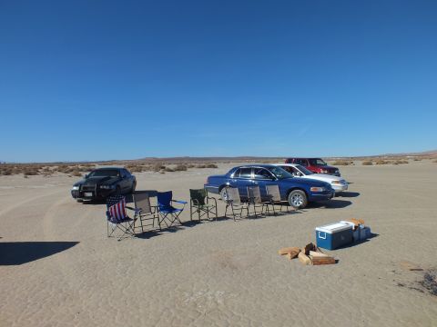 2003 Ford Crown Victoria - Black, blue and red vehicles parked in a row with lawn chairs and a blue cooler on a desert flat.