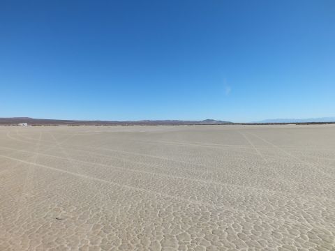 2003 Ford Crown Victoria - Open cracked desert flat marked with looping tire tracks stretching to low distant hills.