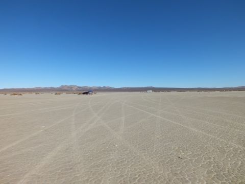 2003 Ford Crown Victoria - wide cracked desert flat with faint vehicle tracks and a far rocky ridge under clear sky.