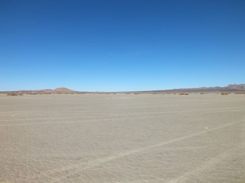 2003 Ford Crown Victoria - Empty cracked desert flat with a lone low hill and distant ridge beneath a clear blue sky.