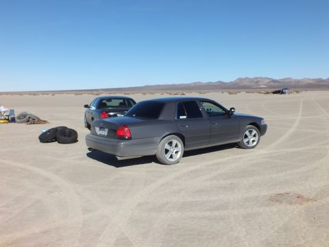 2003 Ford Crown Victoria - Gray Crown Victoria parked on the dry lakebed, loose tires and another sedan visible in the background.