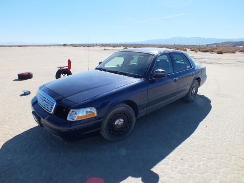 2003 Ford Crown Victoria - Blue Crown Victoria front quarter on the lakebed, black steel spare wheel fitted to the front, mountains behind.