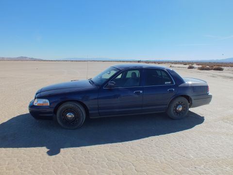 2003 Ford Crown Victoria - Driver-side profile of a blue Crown Victoria fitted with black steel wheels on flat cracked playa.