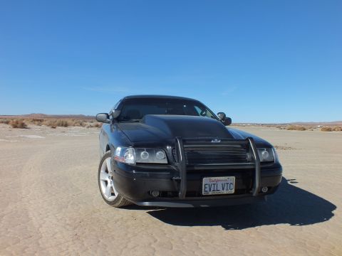 2003 Ford Crown Victoria - Black Crown Victoria with brush guard and projector headlights, EVIL VIC plate, parked on cracked lakebed.