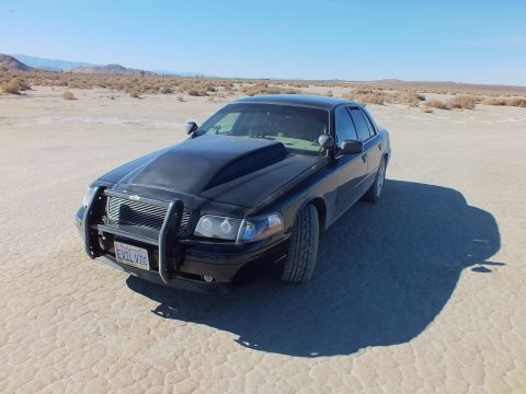 2003 Ford Crown Victoria - Black Crown Victoria with chrome guard casting a long shadow on the playa, EVIL VIC California plate.