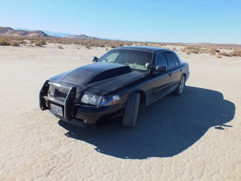 2003 Ford Crown Victoria - Front quarter of the black Crown Victoria with brush guard on cracked playa, low desert hills in distance.