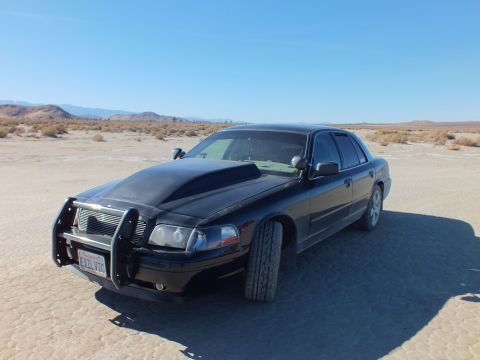 2003 Ford Crown Victoria - Black Crown Victoria with chrome brush guard parked on sunlit playa, mountains along the horizon.