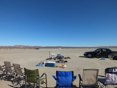 2003 Ford Crown Victoria - Wide playa scene with folding chairs, coolers and gear, a dark Crown Victoria parked to the right.