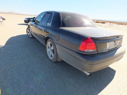 2003 Ford Crown Victoria - Black Crown Victoria photographed from the rear quarter, dusty rocker panels, parked on flat desert lakebed.
