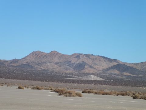 2003 Ford Crown Victoria - Low rocky mountain range above a brush-speckled desert flat, clear blue sky overhead.