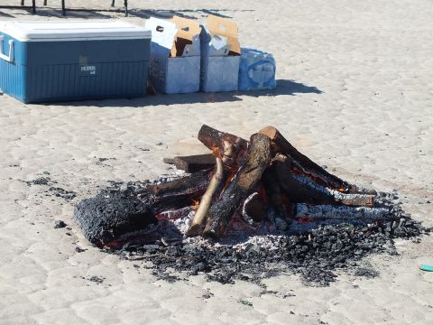 2003 Ford Crown Victoria - Logs burning in a sand fire pit, a blue Thermos cooler and cases of bottled water set behind it.