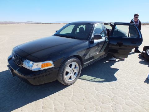 2003 Ford Crown Victoria - Black Crown Victoria front quarter, Ford grille emblem visible, a rear door open with a person standing beside it.
