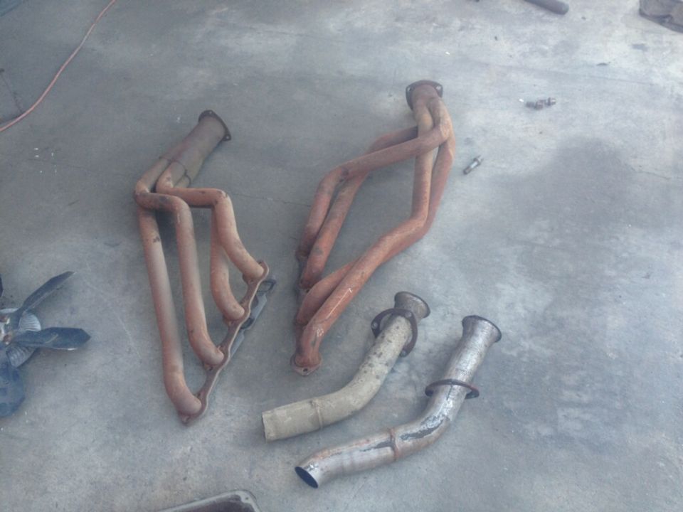 Two rusty exhaust headers and two exhaust pipes on a concrete floor