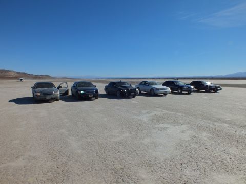 2003 Ford Crown Victoria - Six sedans, several appearing to be Crown Victorias, parked in a diagonal row on the dry lakebed.