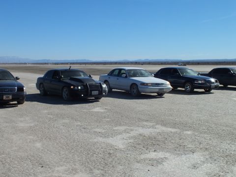 2003 Ford Crown Victoria - black Dodge Charger and several Crown Victoria sedans parked side by side across a desert lakebed.