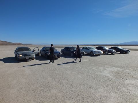 2003 Ford Crown Victoria - Six sedans parked in a row across the lakebed as two people walk between the cars and the camera.