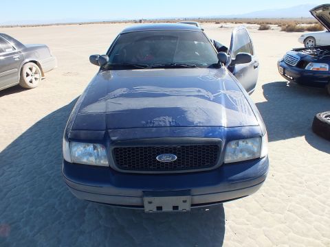 2003 Ford Crown Victoria - Blue Crown Victoria front view, Ford grille emblem and patches of primer on the hood, parked on a lakebed.