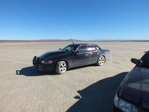 2003 Ford Crown Victoria - Black full-size sedan, appearing to be a Mercury Grand Marquis, parked at an angle on the open lakebed.