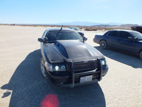 2003 Ford Crown Victoria - Front view of a modified black Crown Victoria, EVIL VIC California plate, parked on a dry lakebed with cars nearby