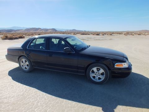 2003 Ford Crown Victoria - Passenger-side view of a black Crown Victoria sedan parked on a dry lakebed, distant mountains
