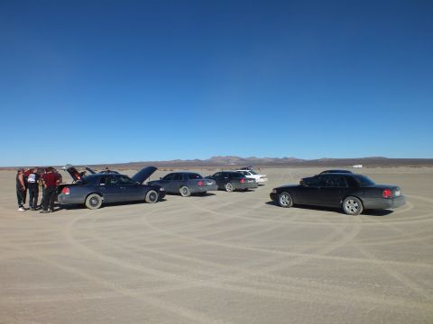 2003 Ford Crown Victoria - Line of sedans with hoods raised and people working at left on a flat dry lakebed