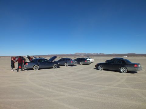 2003 Ford Crown Victoria - Sedans lined up with hoods open and an orange cone, people gathered at left on a dry lakebed