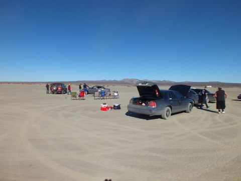 2003 Ford Crown Victoria - People and sedans spread across a dry lakebed with chairs and a red cooler in foreground