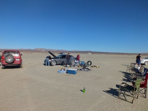 2003 Ford Crown Victoria - Group works around a gray sedan with red SUV at left, cooler and tire on the dry lakebed